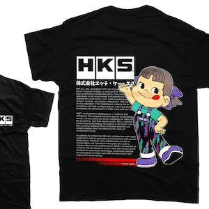 May include: Black t-shirt with a white HKS logo and a cartoon illustration of a girl wearing a blue and purple jumpsuit with the text "HKS" on it. The text "株式会社 エッチ・ケー・エス" is also on the shirt.