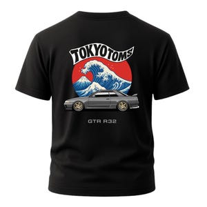 May include: Black t-shirt featuring a graphic of a gray sports car with gold rims, set against a red circle with a blue wave and mountain design. The text "TOKYO TOMS" arches above the wave, and "GTR R32" is below the car.