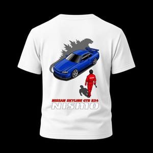 May include: White t-shirt featuring a blue Nissan Skyline GTR R34 car graphic with a Godzilla silhouette and a red racing suit figure. The text "NISSAN SKYLINE GTR R34 NISMO" is printed below the car.