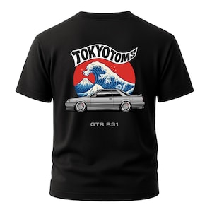 May include: Black t-shirt featuring a graphic design with the text "TOKYO TOMS" above a red circle with a blue wave and a silver car. The text "GTR R31" is below the car.