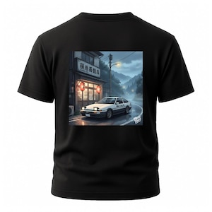 Puede incluir: Camiseta negra con un gráfico detallado de un coche deportivo blanco y negro estacionado frente a un restaurante japonés. La escena está ambientada en una carretera mojada con un fondo montañoso. El texto "TOKYO TOMS" es visible.
