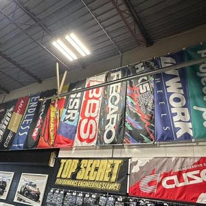 May include: A wall with a variety of colorful banners featuring brand names like Project Mu, Work, Endless, and Top Secret. The banners are hung in a garage or workshop setting.