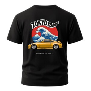 Puede incluir: Camiseta negra con un diseño de coche Fairlady 350Z amarillo. El diseño incluye un círculo rojo, una ola azul y el texto "TOKYO TOMS" encima del coche. El texto "FAIRLADY 350Z" está debajo.