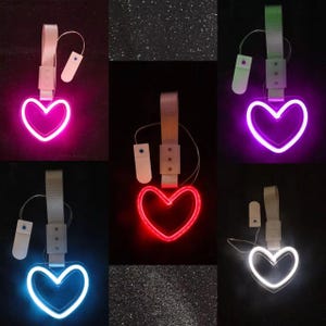 Può includere: Una collezione di luci a LED a forma di cuore in vari colori, tra cui rosa, viola, rosso, blu e bianco. Ogni luce ha un cinturino bianco e una piccola scatola di controllo. Le luci sono esposte su uno sfondo scuro.