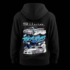 May include: Black hoodie with a graphic of two stylized cars, the text "Silvia" and "Tokyo Toms" in white and blue. The cars have colourful anime-style designs and smoke effects.