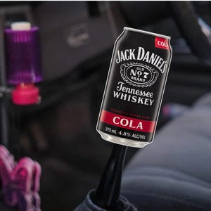 May include: A black can of Jack Daniel's Tennessee Whiskey mixed with cola. The can features the brand's logo and text, including "COLA" in a red banner. The can contains 375 ml and 4.8% alcohol.