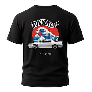 May include: Black t-shirt featuring a graphic of a white car with the text "RX-7 FC" below it. Above the car is a design of a wave, a mountain, and the text "TOKYO TOMS" in white.