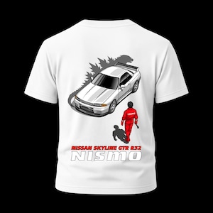 May include: White t-shirt featuring a graphic of a white Nissan Skyline GTR R32 car with a person in a red racing suit. The text "NISSAN SKYLINE GTR R32" and "NISMO" are printed in white.