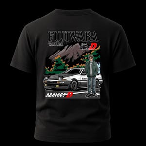 Op de afbeelding: Zwart t-shirt met een grafisch ontwerp met een auto, een persoon en tekst. De tekst bevat "FUJIWARA", "TAKUMI" en "PROJECT-D". De auto is wit en zwart en de persoon draagt een groene jas.