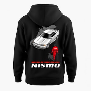 May include: Black hooded sweatshirt featuring a white Nissan Skyline GTR R32 car graphic with a red figure and the text "NISMO". The design includes the text "NISSAN SKYLINE GTR R32". The sweatshirt is made of a soft material.