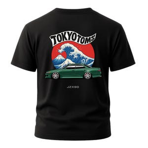 May include: Black t-shirt featuring a graphic design with the text "TOKYO TOMS" above a red circle with a blue wave and a mountain. Below is a green car with the text "JZX90".