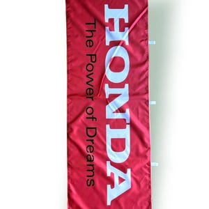 May include: A red banner featuring the word "HONDA" in large white letters and the text "The Power of Dreams" in smaller white letters. The banner has white tabs and a pink string.