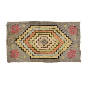 May include: Rectangular rug with a gray background and a central geometric design in shades of orange, yellow, and green. The rug features a cross-shaped design in the center and pink floral accents on each corner.