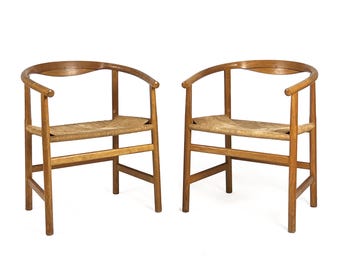 Op de afbeelding: Twee houten stoelen met gebogen rugleuningen en gevlochten rieten zittingen. De stoelen hebben een eenvoudig, minimalistisch ontwerp.