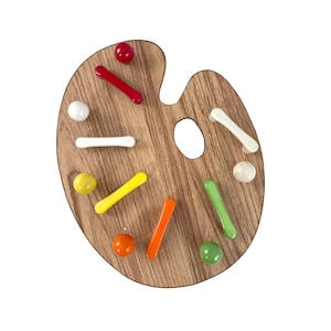 May include: A wooden artist's palette with colorful, rounded paint blobs and brushstroke-shaped accents in red, yellow, orange, green, and white. The palette has a natural wood grain finish and a thumb hole.