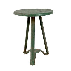 May include: A small, round, green side table with three legs. The tabletop is circular and painted green, showing signs of wear. The legs are also green and have a tripod design, with a decorative base. The table is likely made of metal.