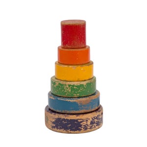 May include: A vintage wooden stacking toy with a red top, followed by orange, yellow, green, blue, and brown rings. The toy has a distressed, worn appearance, suggesting it is an antique or a well-loved item. The toy is designed for children.