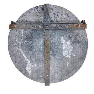 May include: A circular, weathered metal lid with a cross-shaped metal reinforcement. The lid has a distressed, mottled appearance with rust-colored accents on the metal straps. The design suggests a vintage or industrial aesthetic.
