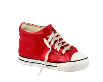 May include: A red ceramic high-top sneaker-shaped planter with white laces and a white toe cap. The planter has a black stripe along the sole and is a decorative item.