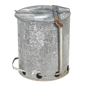 May include: A galvanized metal charcoal chimney with a lid and handle. The cylindrical container has air vents near the base and a hinged lid with a metal handle. The metal has a weathered appearance.