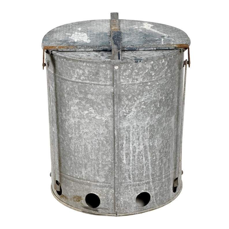 May include: A galvanized metal trash can with a lid. The cylindrical can has a handle on the lid and two circular holes near the bottom. The metal has a weathered appearance.