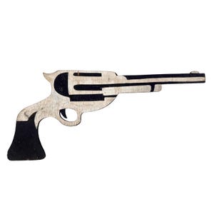 May include: A flat, two-dimensional cutout of a revolver silhouette crafted from wood. The object features a high-contrast design with natural light-colored wood grain sections alternating with solid black painted areas on the handle and cylinder.