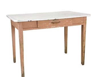 Könnte beinhalten: Ein Vintage-Schreibtisch mit weißer Tischplatte und einer Schublade. Der Schreibtisch hat einen verwitterten, rosa-braun lackierten Rahmen und Beine. Die Schublade hat einen Holzgriff. Der Schreibtisch ist ca. 102 cm lang.