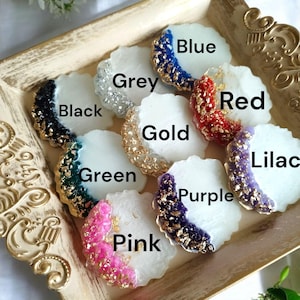 Pode incluir: Uma cole&ccedil;&atilde;o de bases decorativas em v&aacute;rias cores, incluindo azul, cinza, preto, dourado, vermelho, verde, rosa, roxo e lil&aacute;s. Cada base tem uma base branca com uma borda colorida e texturizada e detalhes dourados. As bases s&atilde;o exibidas em uma bandeja dourada.