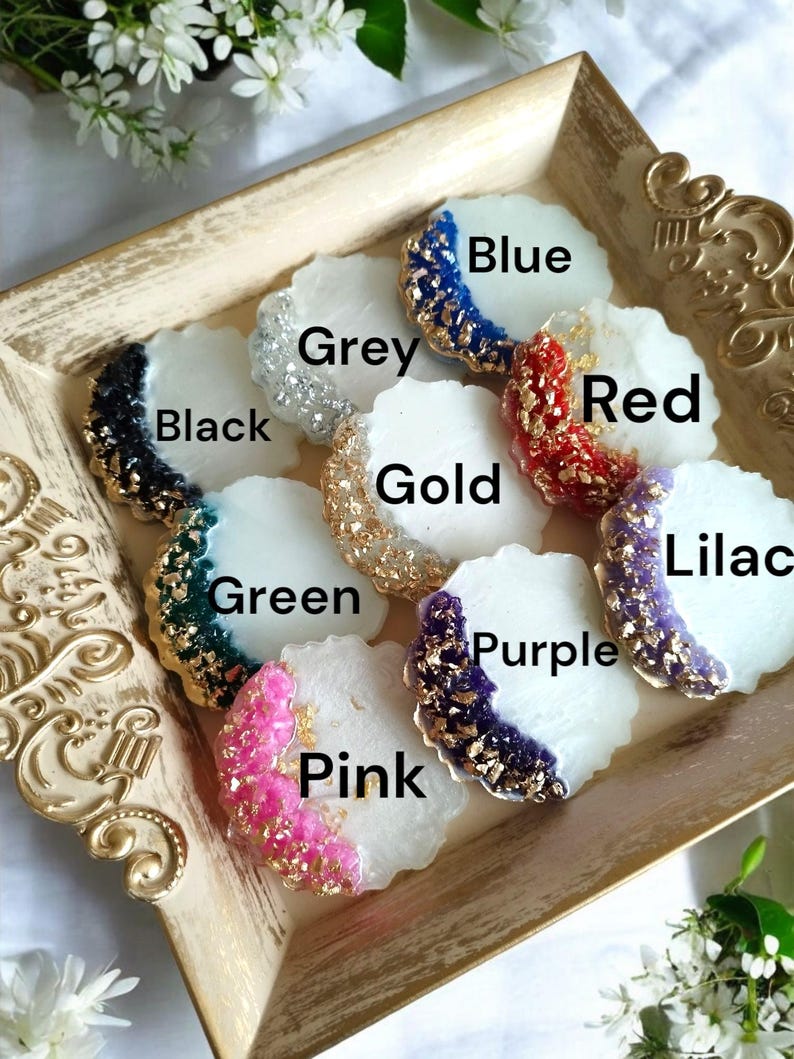 Pode incluir: Uma cole&ccedil;&atilde;o de bases decorativas em v&aacute;rias cores, incluindo azul, cinza, preto, dourado, vermelho, verde, rosa, roxo e lil&aacute;s. Cada base tem uma base branca com uma borda colorida e texturizada e detalhes dourados. As bases s&atilde;o exibidas em uma bandeja dourada.