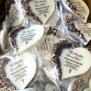 May include: Heart-shaped cookies with a white base and a decorative edge of gold and purple accents. Each cookie is individually wrapped and features the text "The Steadfast Love of God" and other text.