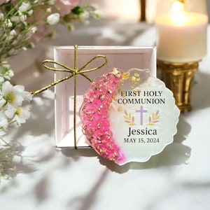 May include: A white and pink resin keepsake with gold glitter. The keepsake has a cross and the text "FIRST HOLY COMMUNION Jessica MAY 15, 2024".