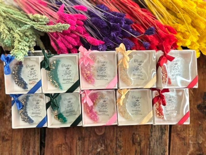 Pode incluir: Caixas de presente com itens decorativos com glitter, amarradas com fitas coloridas. O texto "Frisks 55th Birthday" est&aacute; impresso em cada caixa. Flores secas coloridas no fundo.
