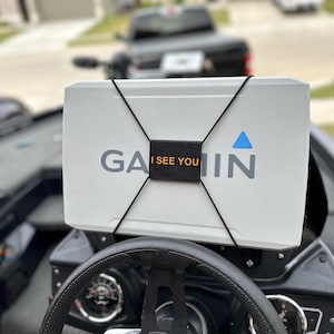 May include: A white Garmin fish finder with a black strap and the text "I See You" is mounted on a black boat dashboard.