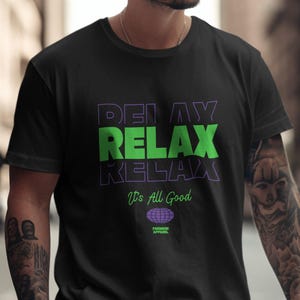 Puede incluir: Camiseta negra con un gráfico verde y morado que dice "Delay Relax Relax" y "It's All Good". El gráfico también incluye un pequeño logotipo de globo terráqueo con el texto "Premium Apparel".