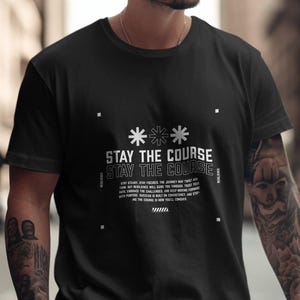 May include: Black t-shirt with a white graphic print that says "Stay the Course" and includes a motivational quote. The quote reads "Stay steady, stay focused. The journey may twist and turn, but resilience will guide you through. Trust your path, embrace the challenges, and keep moving forward with purpose. Success is built on consistency and effort. Finding the course is how you'll conquer."