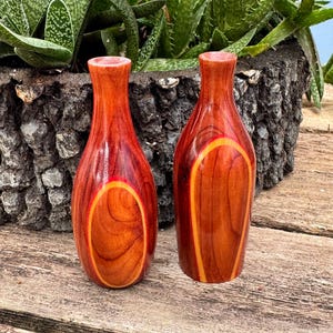 May include: Two handcrafted wooden vases with a rich reddish-brown hue and a contrasting yellow-orange oval design. The vases have a smooth, polished finish and a slender neck, perfect for displaying small flowers or as decorative accents.