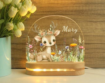 May include: A decorative night light featuring a cartoon deer with floral accents and the name "Mary". The deer is set against a backdrop of colorful wildflowers and illuminated by warm LED lights within a wooden base.