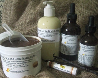 Può includere: Una collezione di prodotti di bellezza naturali di Meadow Muffin Gardens, tra cui uno scrub allo zucchero di canna, un balsamo per labbra alla vaniglia, una lozione per il corpo, un olio da massaggio e un balsamo per capelli. I prodotti sono esposti su uno sfondo di juta con baccelli di vaniglia.