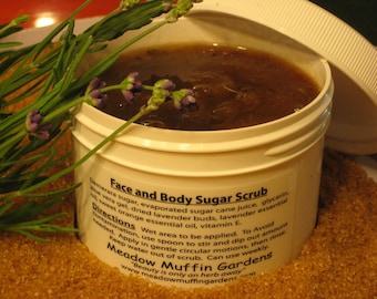 May include: A white jar with a brown sugar scrub inside. The jar has a label that reads "Face and Body Sugar Scrub" and "Meadow Muffin Gardens". The jar is surrounded by brown sugar crystals.