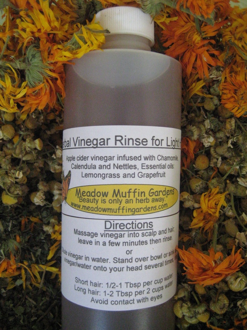 Może przedstawiać: Brązowa szklana butelka z białym korkiem, z etykietą "Herbal Vinegar Rinse for Light Hair". Etykieta zawiera listę składnik&oacute;w, w tym ocet jabłkowy, rumianek, nagietek, pokrzywę, trawy cytrynowej i grejpfruta. Butelka jest otoczona suszonymi kwiatami.