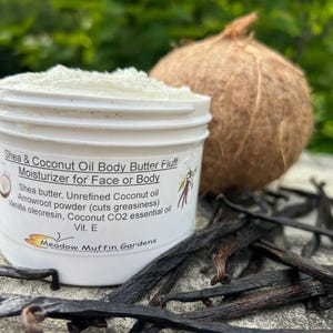 May include: A white plastic tub filled with Shea & Coconut Oil Body Butter Fluff moisturizer for face or body. The label lists ingredients including shea butter, unrefined coconut oil, arrowroot powder, vanilla oleoresin, and vitamin E.