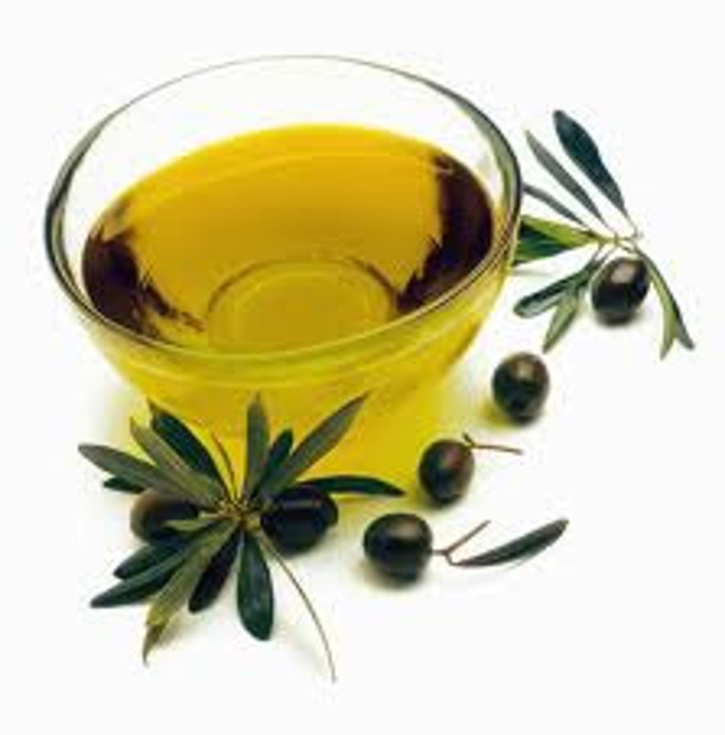 May include: A clear glass bowl filled with golden yellow olive oil, surrounded by green olive branches and black olives.