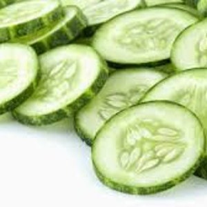May include: Close-up of several thin slices of fresh green cucumber, arranged in a pile on a white background.
