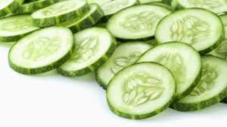 May include: Close-up of several thin slices of fresh green cucumber, arranged in a pile on a white background.