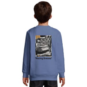 Könnte beinhalten: Ein blaues Langarmshirt mit einem Schwarzweißfoto eines Autos auf der Rückseite. Das Foto ist von einem goldenen Rahmen umgeben. Der Text "Racing Dreams" ist unter dem Foto gedruckt.