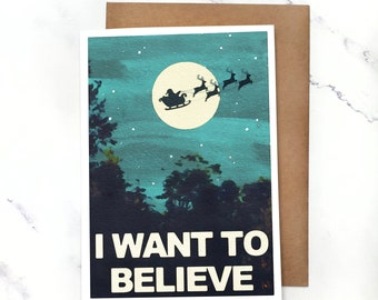 May include: A Christmas card with a blue and green watercolor background featuring a silhouette of Santa Claus flying in a sleigh pulled by reindeer in front of a full moon. The text "I WANT TO BELIEVE" is printed in white on a black background at the bottom of the card.