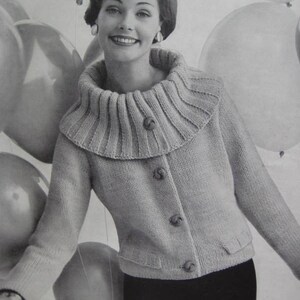 Peut inclure: Une femme portant un cardigan en tricot gris clair avec un large col plié et quatre boutons. Le cardigan a deux poches plaquées sur le devant. La femme est entourée de ballons.