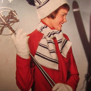 May include: A woman wearing a white and black striped knit hat with a pom pom, a white and black striped scarf, and a red jacket. She is holding ski poles and is wearing white gloves.