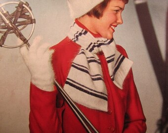 Peut inclure: Une femme portant un bonnet en tricot blanc et noir à pompon, une écharpe blanche et noire à rayures et une veste rouge. Elle tient des bâtons de ski et porte des gants blancs.