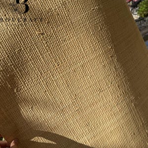 May include: A roll of woven natural fiber material in a light tan color. The material has a textured, grid-like pattern. The upper left corner displays the text "BOUGCRAFT" with a stylized "B" logo. The material is being held by a hand.
